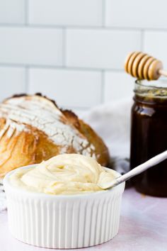 a jar of honey sits next to some bread on a table with a spoon in it