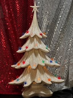 a white ceramic christmas tree sitting on top of a table next to a red curtain