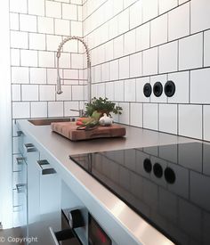 a kitchen with black counter tops and white tiles on the wall behind it is a cutting board that holds vegetables