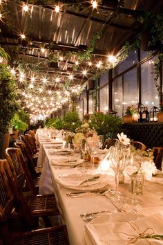 an indoor dining area with tables and chairs covered in white tablecloths, lit by fairy lights