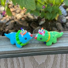 two toy dinosaurs sitting on top of a wooden bench