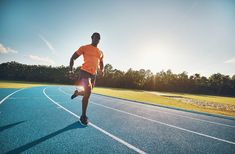 a man running on a blue track in the sun with trees in the back ground