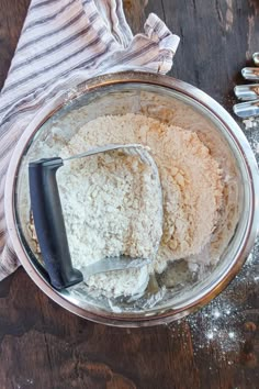 a metal bowl filled with white rice on top of a wooden table next to utensils