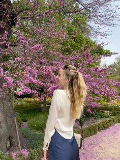 a woman standing in front of a tree with pink flowers