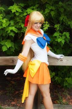 a woman dressed in an orange and white outfit with long blonde hair, posing on a wooden bench