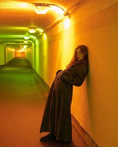 a woman leaning against a wall in a long hallway with neon lights on the walls