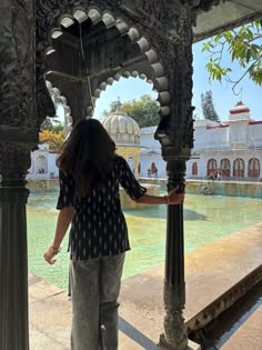 a woman standing in front of an ornate gazebo next to a body of water