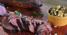 a wooden cutting board topped with sliced up meat and garnished with corn kernels