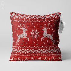 a red and white knitted christmas pillow with reindeers on it, sitting against a gray background