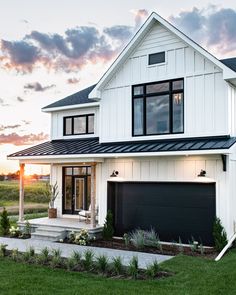 a white house with black garage doors and windows on the front porch at sunset or dawn