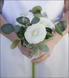 a woman holding a bouquet of white flowers and greenery on her wedding day,