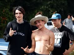 three shirtless men standing next to each other in front of a blue pickup truck