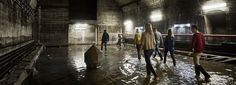 several people walking through a flooded subway station at night time, with lights on and one person in the middle of the tunnel