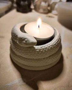 a lit candle sitting on top of a table next to a snake wrapped around it