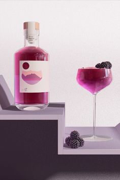 a bottle of booze next to a glass filled with blackberries and raspberries