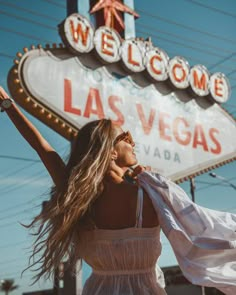 a woman in a white dress is holding her arms up and smiling at the las vegas sign