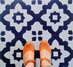 a woman's feet in orange shoes standing on a tiled floor