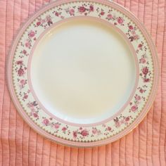 a pink and white plate with flowers on it sitting on a quilted tablecloth