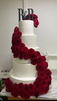 a three tiered white cake with red roses on it and the initials r & b