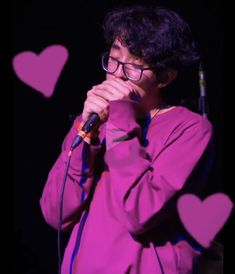 a man with glasses holding a microphone in front of heart shaped paper cutouts