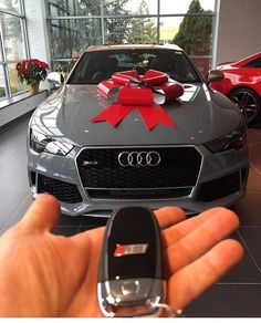 a hand holding a car key in front of a gray audi with a red bow on it