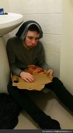 a man sitting on the toilet with a pizza in his hand and wearing a hoodie