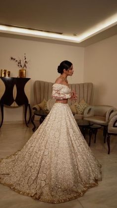 a woman in a wedding dress standing in a room with couches and chairs behind her