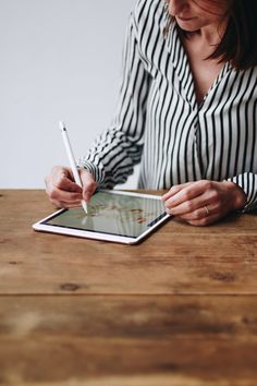 a woman sitting at a table writing on an ipad with a pen in her hand