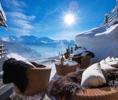 the sun shines brightly over an outdoor area with wicker furniture and snow covered mountains in the background