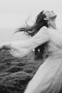 a woman with her arms spread out in the air while standing on top of a grass covered field