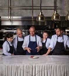 five chefs standing in front of a white table with food on it and one man pointing at the plate