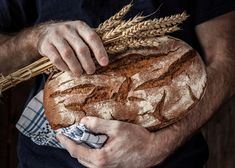 a man holding a loaf of bread with ears of wheat in his hands on top of it