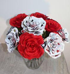 a glass vase filled with red and white flowers on top of a wooden table next to a wall