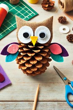 an owl made out of pine cones sitting on top of a table next to scissors