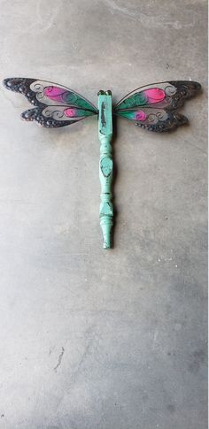 a green and pink dragonfly sitting on top of a cement floor