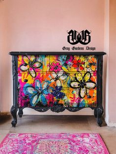 a colorful dresser with flowers painted on the front and bottom, along with a pink rug