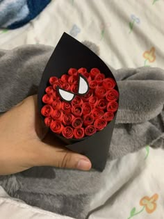 a hand holding a black box with red roses in the shape of a spider man