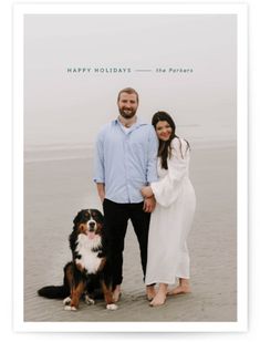 a man and woman standing next to a dog on the beach