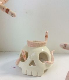 a white ceramic skull with two hands reaching for it's mouth and another hand holding a pen