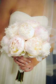 a bride holding a bouquet of white and pink peonies