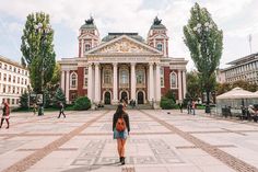 a woman standing in front of a building with columns and arches on the top floor