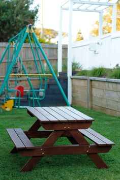 a wooden picnic table sitting on top of a lush green field next to a playground