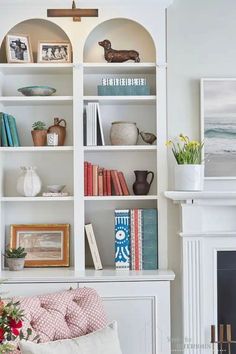 a living room filled with lots of white furniture and bookshelves next to a fire place