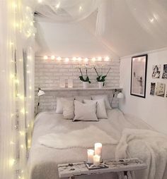 a bedroom with white bedding and lights on the ceiling, along with candles in vases