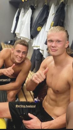 two men sitting next to each other in a locker room with shirts hanging on the wall