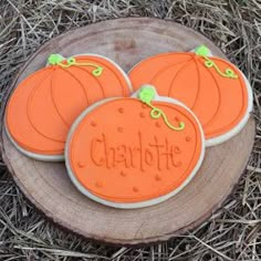 three decorated cookies sitting on top of a wooden slice in the grass next to some dry grass