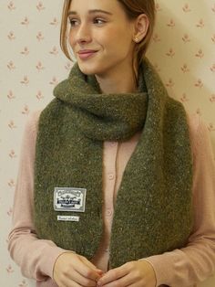 a woman standing in front of a wall wearing a green scarf