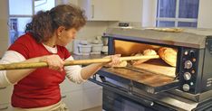 a woman holding a wooden stick in front of an oven with bread baking on it