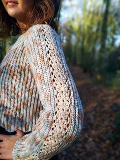 a woman standing in the woods with her hands on her hips wearing a knitted sweater