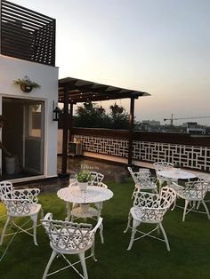 an outdoor patio with white chairs and tables on the grass, next to a building